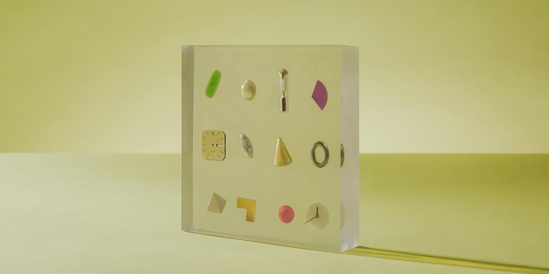 A transparent cube contains clock parts and miscellaneous shapes.